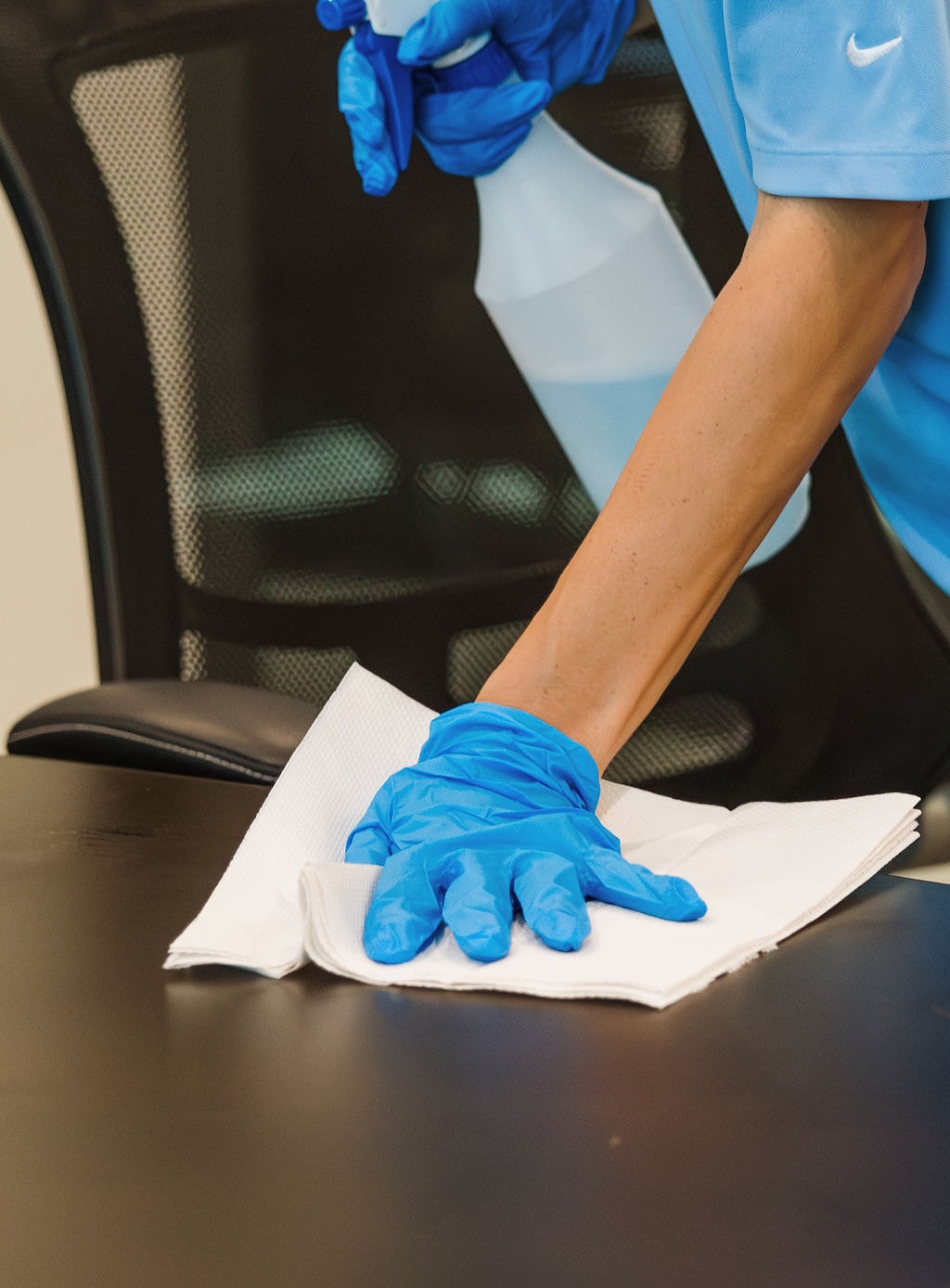 Gloved hand wiping a dark, glossy tabletop with a cloth
