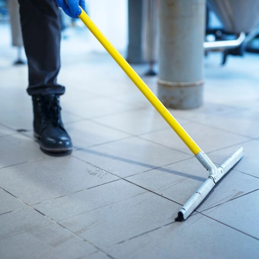 Close-up of a floor squeegee being pushed across a light tile floor